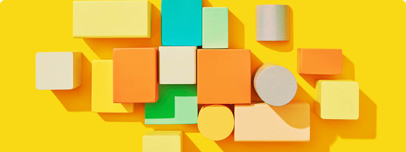Geometrical pattern from multicolored wooden cubes and blocks different size and shapes on a yellow background with hard shadows, copy space. Teamwork project collaboration business concept. Top view.
